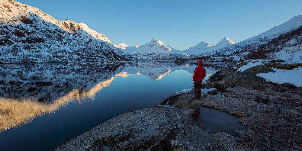 person in red hoodie looking into the snowed mountains and undisturbed lake